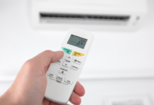 Person using an air conditioner remote control to adjust the temperature for better energy efficiency and lower AC electricity bills during hot summer weather.