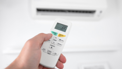 Person using an air conditioner remote control to adjust the temperature for better energy efficiency and lower AC electricity bills during hot summer weather.