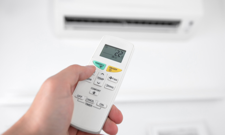 Person using an air conditioner remote control to adjust the temperature for better energy efficiency and lower AC electricity bills during hot summer weather.
